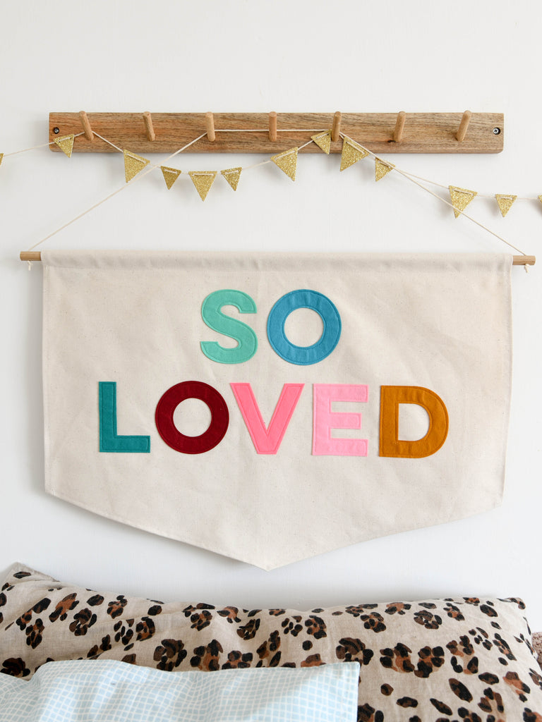 Canvas banner with the words so loved sewn on in coloured felt.