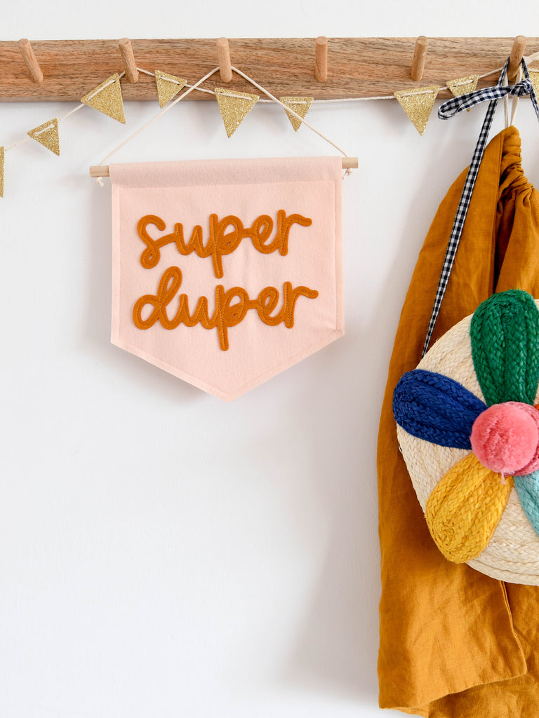 mini felt banner with the words super duper sewn on in cursive text hung from a shelf in a nursery.