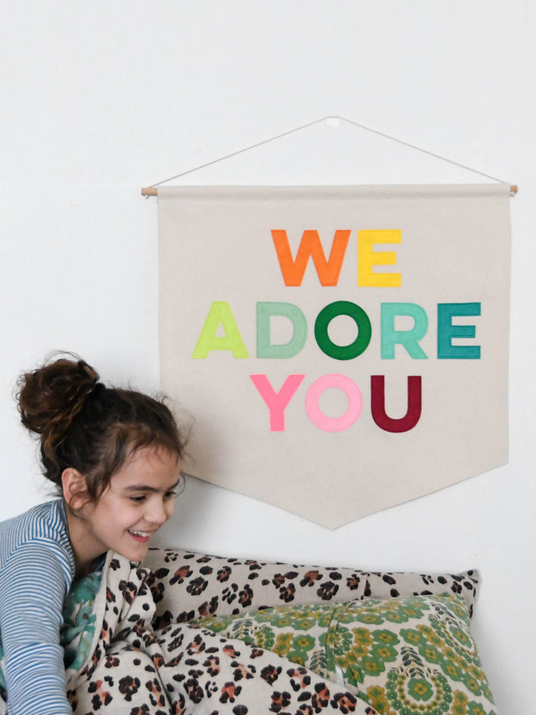 banner with the words we adore you on hung behind a young girl.