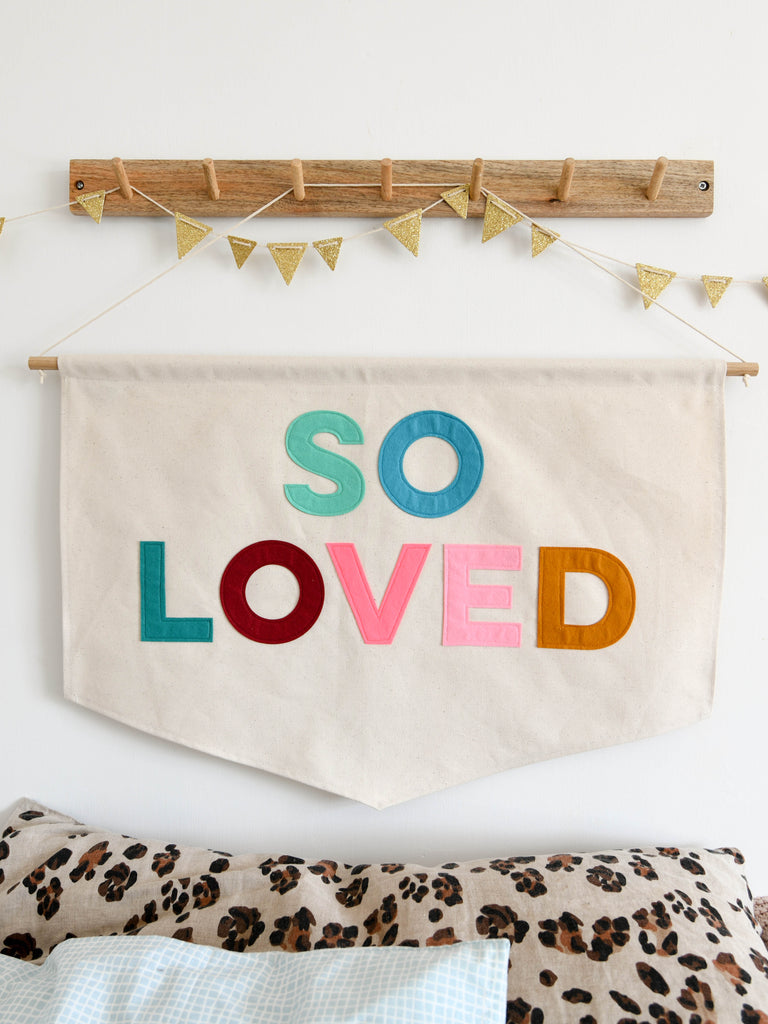 Canvas banner with the words so loved sewn on in coloured felt.