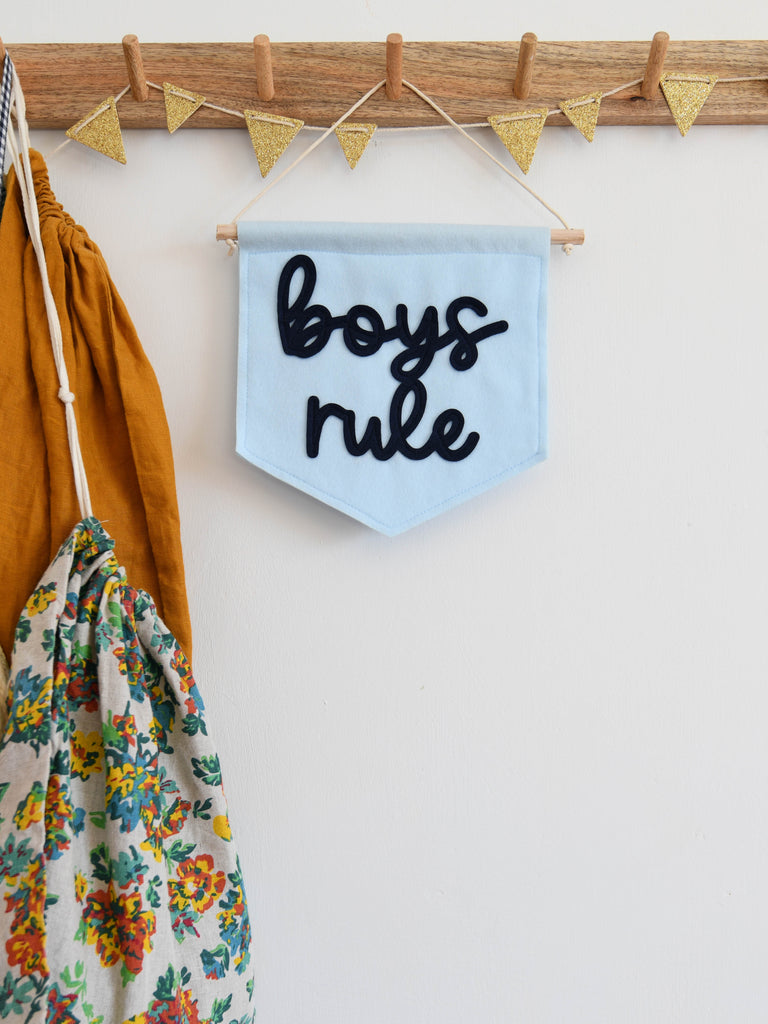 mini felt banner in baby blue with the words boys rule sewn on in cursive font hanging from a kids room shelf.