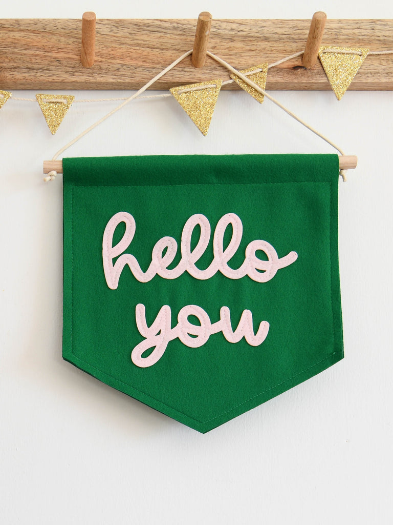 green felt banner with hello you sewn on in pink cursive text.