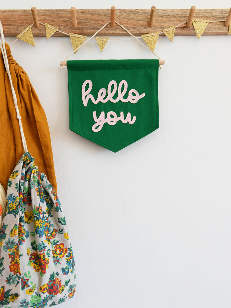 green felt mini banner with hello you written in baby pink felt hung in a hall way to welcome guests.