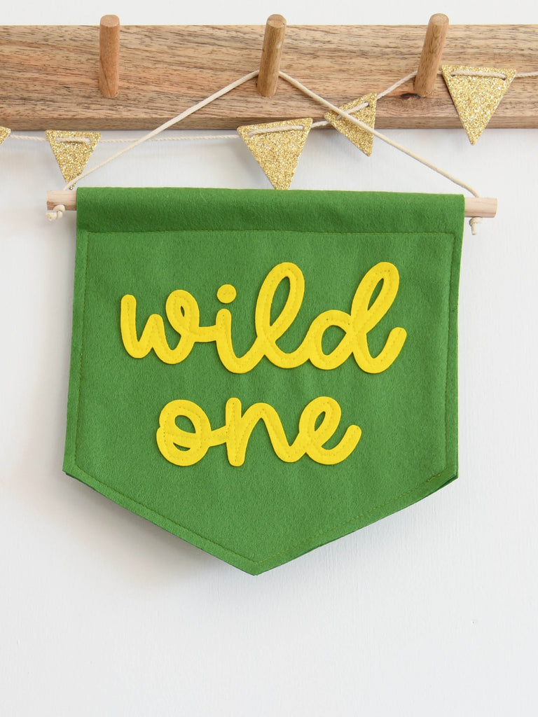 mini green felt banner with wild one sewn on in yellow cursive text.