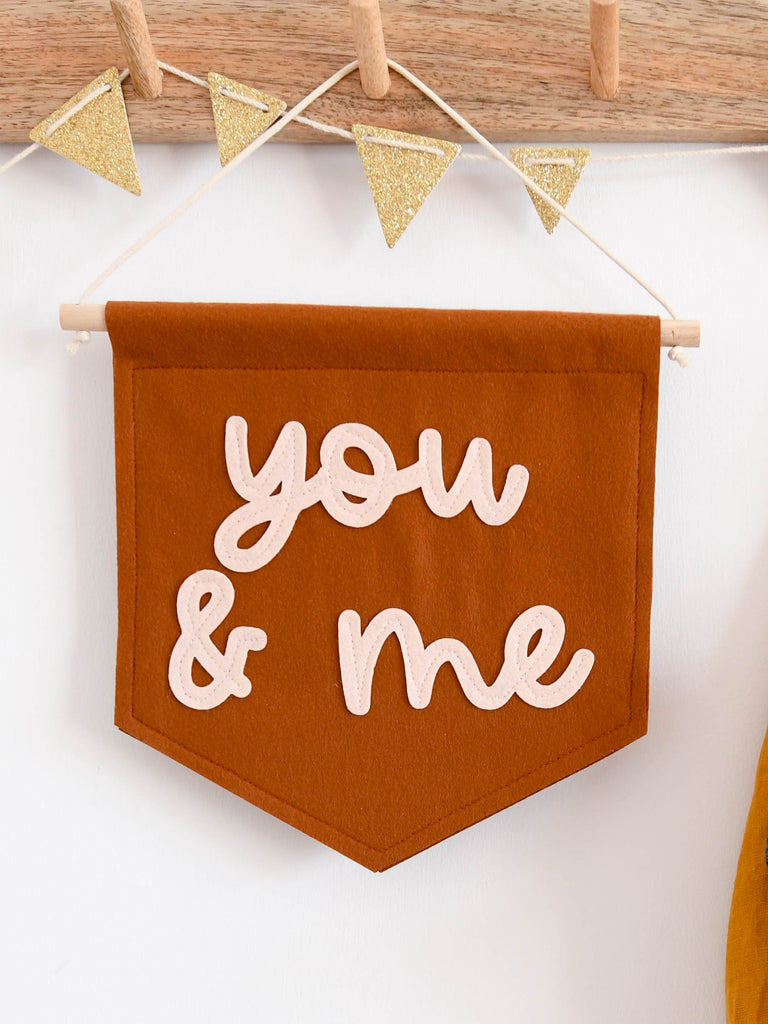 you and me mini felt banner hung on a peg hook.